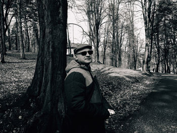 Portrait of man standing by tree trunk in forest