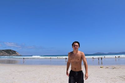 Rear view of man standing at beach against clear blue sky