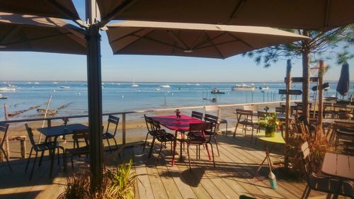Empty chairs and tables at beach against sky