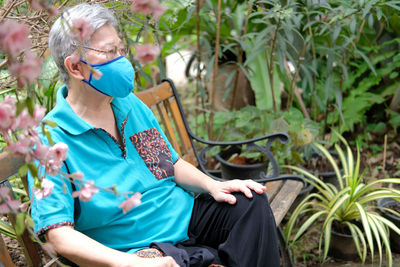 Senior woman wearing mask sitting on bench at park