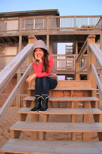 Full length portrait of smiling woman sitting on wooden steps at beach