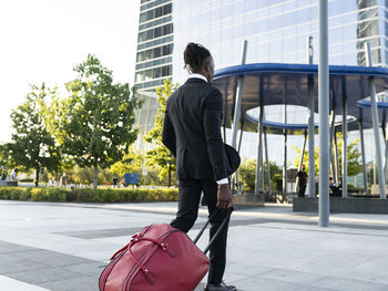 Back view of african american male entrepreneur wearing classy suit walking with suitcase towards airport for departure