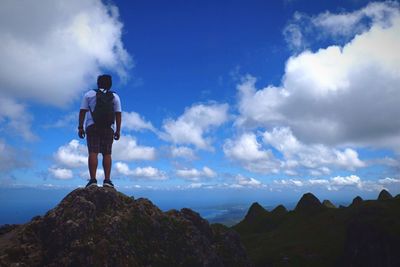 Rear view of man standing on mountain against cloudy sky