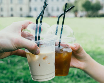 Cropped image of hands toasting iced coffee in disposable cups at park