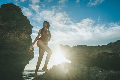 Low angle view of woman standing on rock against sky