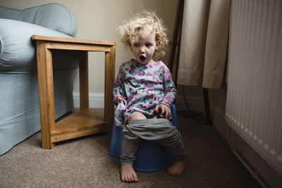 Girl with mouth open sitting on potty in room at home