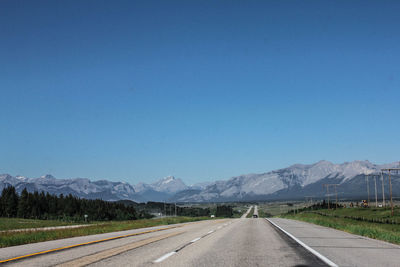 Empty road by mountains against clear blue sky