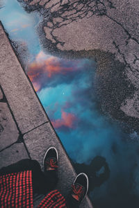 Low section of man standing by puddle on footpath