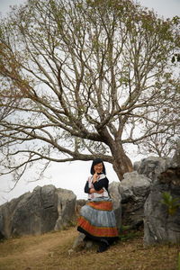 Woman sitting on rock against tree