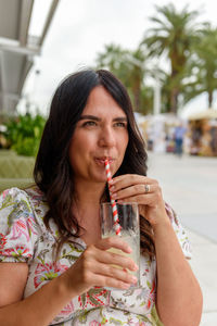 Pretty girl with long hair sitting in bar outdoor in city, drinking lemonade on straw