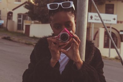 Young woman wearing sunglasses while standing in city holding camera 