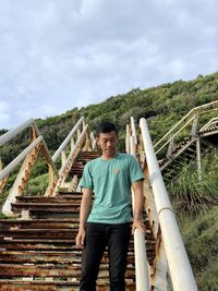 Full length of young man standing on staircase against sky