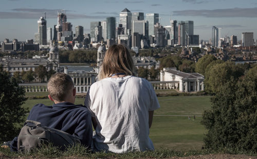 Rear view of people sitting by buildings against sky