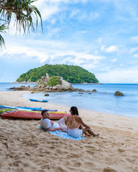 Rear view of woman sitting at beach against sky