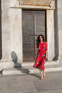 Portrait of smiling young woman standing on one leg against door