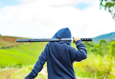 Boy in hooded shirt with sword on field