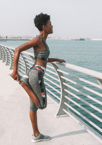 Full length of young woman standing by railing against sea