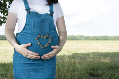 Young pregnant woman in blue sundress with heart shape with flowers. copy space.