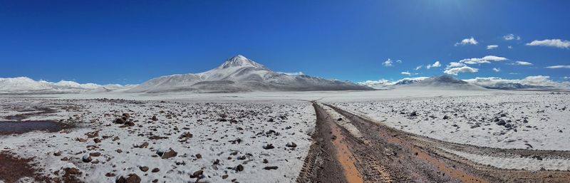 Scenic view of snow covered land against mountains and blue sky