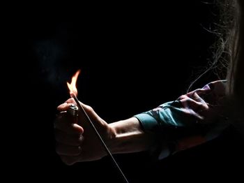 Cropped hand of woman burning incense stick in darkroom