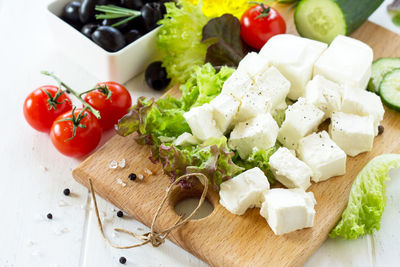 Feta cheese and black olives, cooking qreek salad with fresh vegetables on a white wooden table.