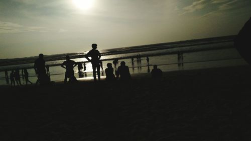 Silhouette people on beach against sky during sunset