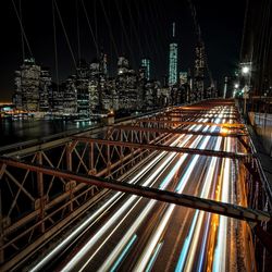 Light trails on bridge over river by buildings at night