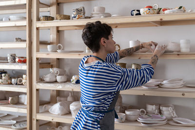 Pottery artist placing clay objects on shelves to dry before firing while working in art studio