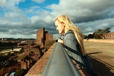 Side view of smiling young woman standing on bridge