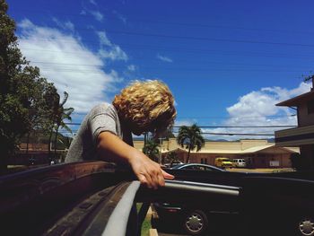 Blond man by car against blue sky