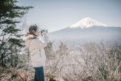 Side view of woman photographing while standing against mountain