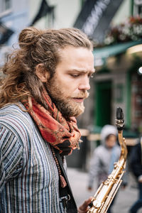 Vertical photo of man with long hair and beard dressed in hippie clothes with a saxophone