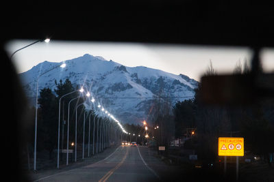 Road by illuminated street against sky at night