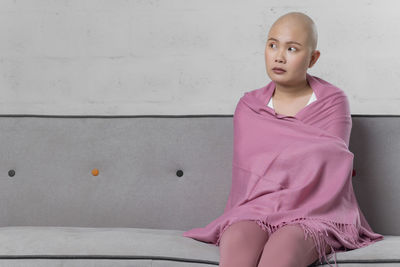 Young woman looking away while sitting against wall