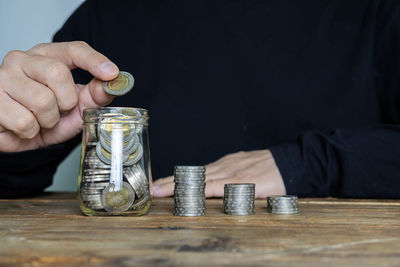 Close-up of hand holding coins in jar on table