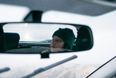 Reflection of young woman on rear-view car mirror