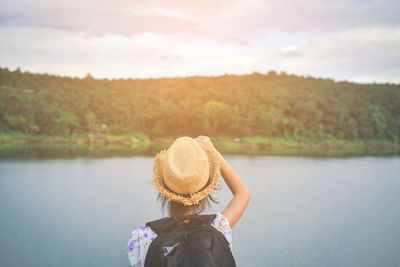 Rear view of woman wearing hat against river at sunset