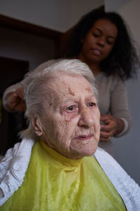 Caring african american woman caregiver, cutting her elderly woman hair at home