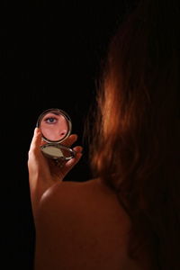 Reflection of woman eye in hand mirror against black background