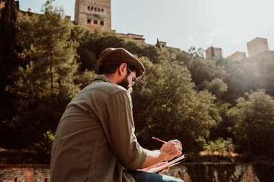 Man writing in notepad against trees