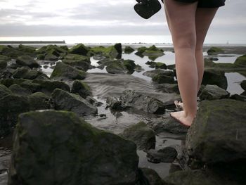 Low section of woman standing on rock against sky