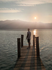 Man standing on pier over lake against sky during sunset