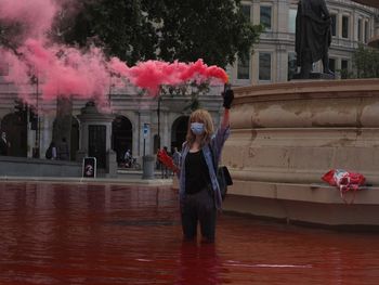 Woman holding red umbrella against building in city