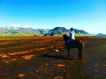 Woman riding horse on field against blue sky