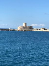 Buildings by sea against blue sky