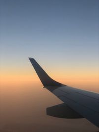 Airplane wing against clear sky during sunset
