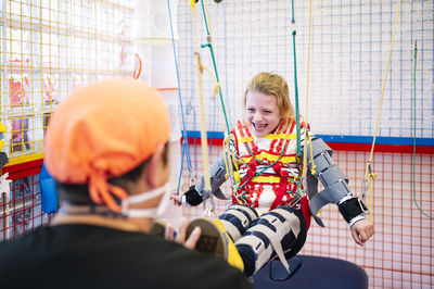 Crop anonymous specialist giving support to girl with angelman syndrome during rehabilitation training with elastic straps