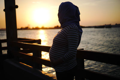 Rear view of woman standing on pier against sky during sunset