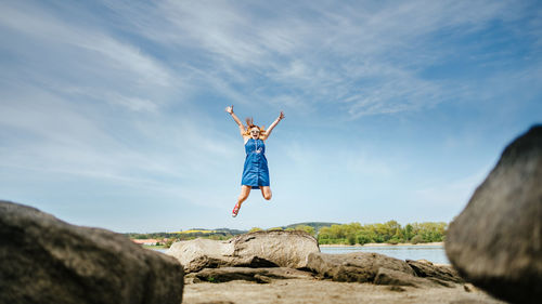 Rear view of man jumping on rock against sky