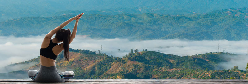 Man with arms raised on mountain against sky